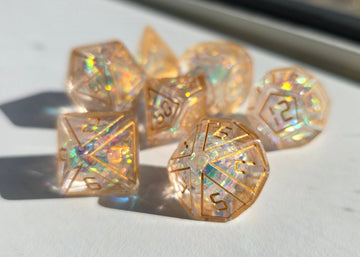 A set of transparent, holographic polyhedral dice resting on a white surface in bright natural sunlight.